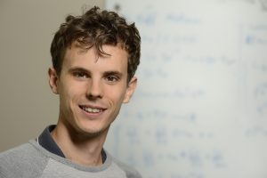 A headshot of Nicolas Charon wearing a gray sweatshirt with blurred background of a white board behind him.