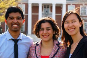 Aditya Mohan, Alaleh Azhir, and Wenzer Qin posing for a picture with the Gilman Hall behind them in the background.