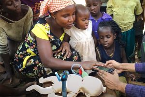 A woman along with kids interacting a mobile and baby simulation model, in Uganda.
