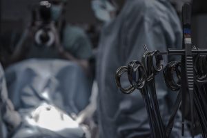 A few of the surgical scissors hung on a stand with blurred background of a surgery going on.