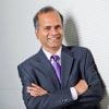 Rama Chellappa wearing a dark blue suit poses for a picture while folding hands.