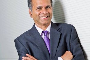 Rama Chellappa wearing a dark blue suit poses for a picture while folding hands.