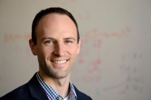 A headshot of Michael Shields with a blurred white board in the background.