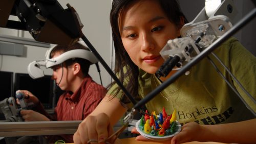 A student making a colorful art sculpture with a magnifying instrument.