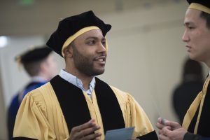 Two students dressed in graduation gown and cap and are talking to each other.