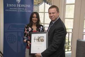 Archana Venkataraman receiving an award from a man with Johns Hopkins banner behind her.