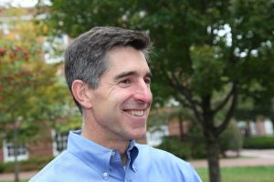 A side headshot of Weihs Timothy wearing a blue shirt and standing outdoors of the campus.