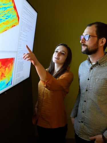 Two people examine graphical representations of data on a big screen.