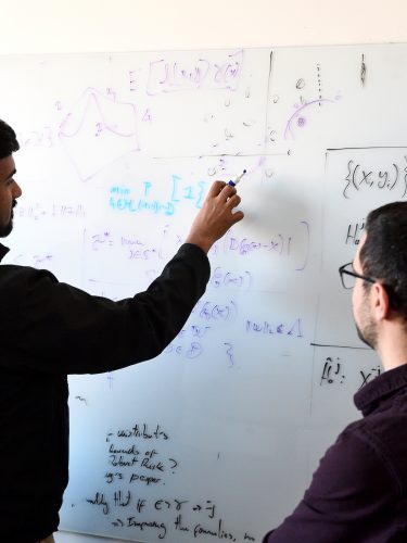 Two students writing equations on a white board.
