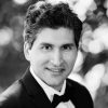 A grayscale headshot of Ali Madooei wearing a suit with a bow tie.