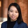 A headshot of Anqi (Angie) Liu wearing a dark blue blazer and standing in the corridors of the campus.