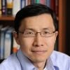 A headshot of Xiangyang Li wearing a light blue shirt with a bookshelf in the background