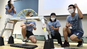 Four students wearing facemask and glasses with a spaghetti bridge that holds weight.
