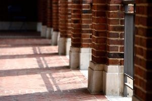 Image of outside colonnade with sun casting shadows on brick floor.
