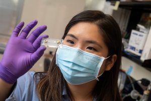 A student examines a vial in her gloved hand.