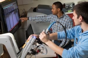 A student utilizes an imagine device while the professor points to observations on a screen.