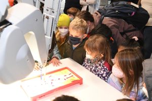 Children watch as a surgical robot demonstrates its work on the board game Operation.