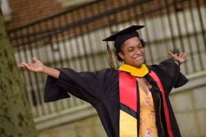 A student in a cap and gown holds her arms out in celebration