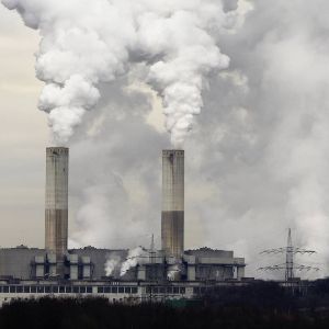A building with two large smokestacks billowing smoke against a gray sky. 