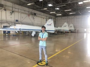 Daniel Chong poses for a photo inside a NASA airplane hanger. Behind him are three planes with the NASA logo on their tails. 