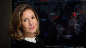 A headshot photo of Lauren Gardner with her COVID-19 dashboard in the background.