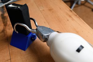 A prosthetic limb grips an item on a table.