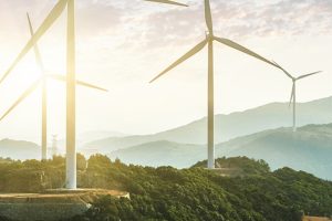 A rendering of wind turbines on a hilly landscape with a sunset in the background.