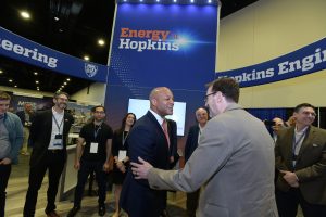 Governor Wes Moore shakes hands with Benjamin Schafer surrounded by Hopkins faculty in a convention booth.
