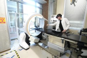 Benjamin Killeen, a PhD student at Johns Hopkins, adjusts a 3D model under a Loop-X medical imagine robot, a ring-shaped device that has an operating table under it.