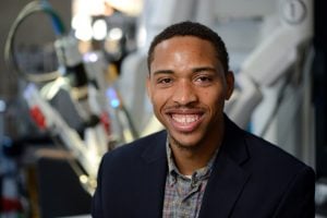 Jeremy Brown poses for a headshot with a surgical robot behind him.