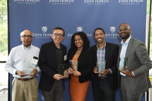 Five Hopkins Engineering staff and faculty pose against a backdrop, holding glass awards.