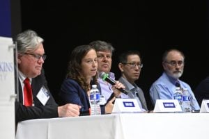 Elizabeth Stuart speaks into a microphone while sitting at a table with other panelists.