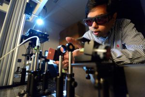 Ishan Barman wears protecting goggles, conducting work on a machine in the laser lab.
