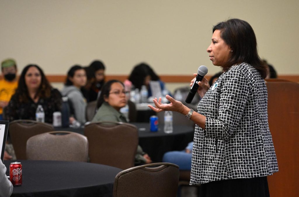 Inez Stewart, holding a microphone, speaking to a room of people.