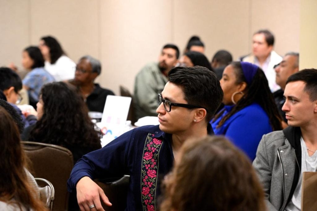A audience sitting at tables looks towards a spaker. 