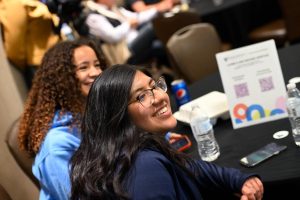 Two women smile while listening to a presenter