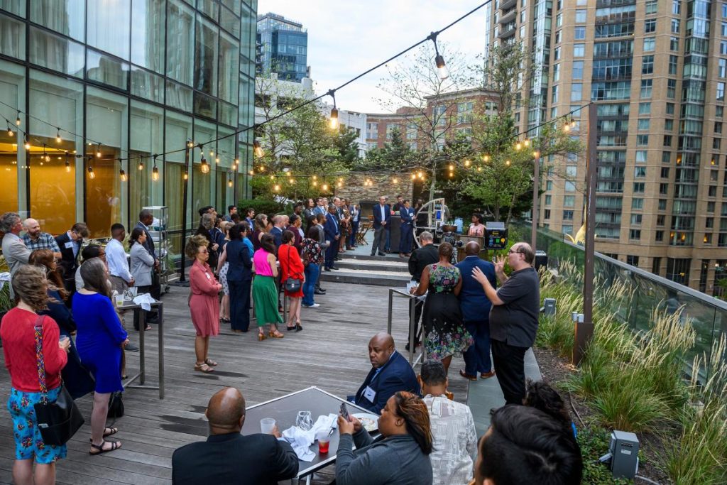 A large gathering on an outdoor terrace, with string lights overhead.