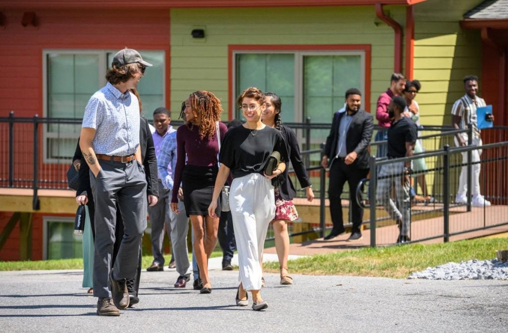 A group of people walk away from a red and yellow building on a sunny day.