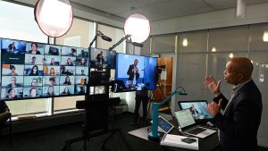 A professor teachers an online course in front of monitors and spotlights.