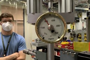 Brett Kuwik poses for a photo next to a machine's pressure gauge showing 3,000 psi.