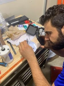 Ghassan Shahin hunches over a desk, manipulating a sample with a tweezer-like instrument. 