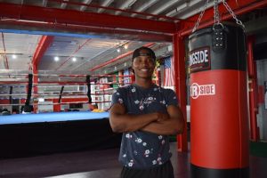 Samson Dessalines poses, arms crossed, next to a heavy bag inside the Corner Team boxing gym. 