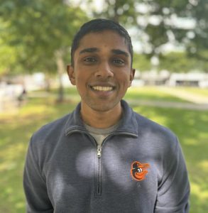 Ashwin Pasupathy smiles for a photo outdoors wearing an Orioles pullover.