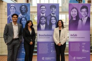 3 members of the Bronchosleeve team pose for a photo at the College Inventors Competition, standing in front of banners highlighting the finalists.