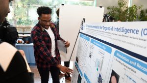 A student gestures towards their poster, in discussion with a poster session attendee.