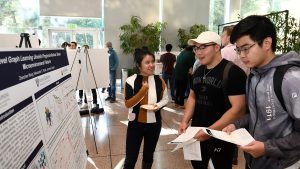 Three students chat while looking at a poster