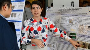 A researcher gestures to her poster as she explains her work to a poster session participant.