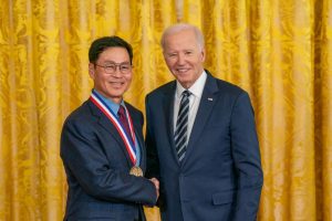 Jeong Kim. wearing a medal, poses for a photo, shaking hands with President Joe Biden.