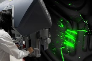 A image combining two photos - a grad student utilizes the interface of the da Vinci robotic surgical system and a close-up view of the robot making florescent sutures.