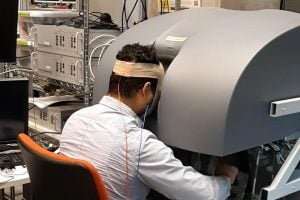 A surgeon trains on a robotic surgery machine with electrodes attached to their head.